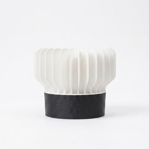 A modern table lamp with a ribbed white shade and a textured black base, photographed against a seamless white background.